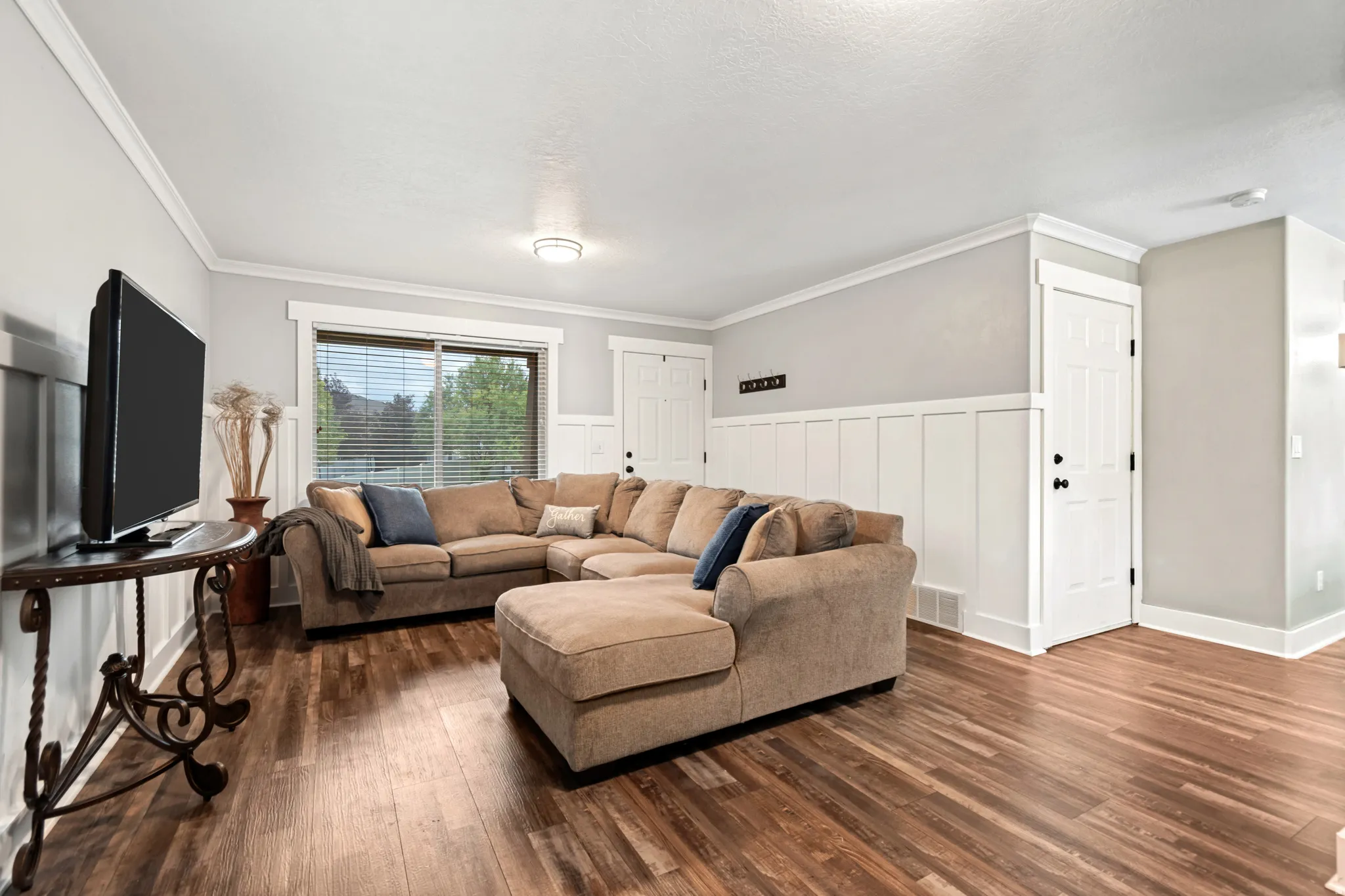 Wood-finish flooring, accent wall with wainscoting, crown molding, modern ceiling light, and white paneled doors