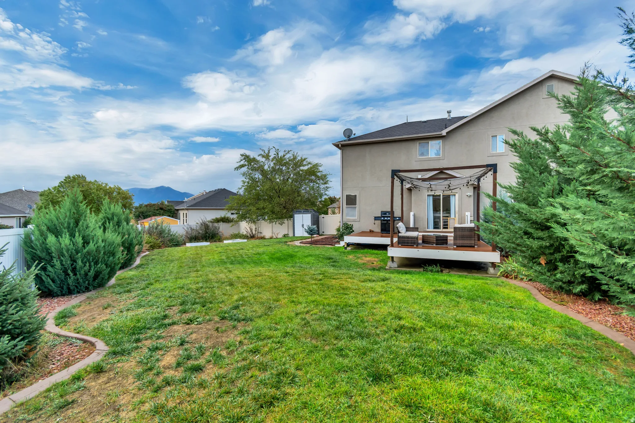 Expansive backyard featuring a large lawn area, wooden deck, pergola structure, and sliding glass door access