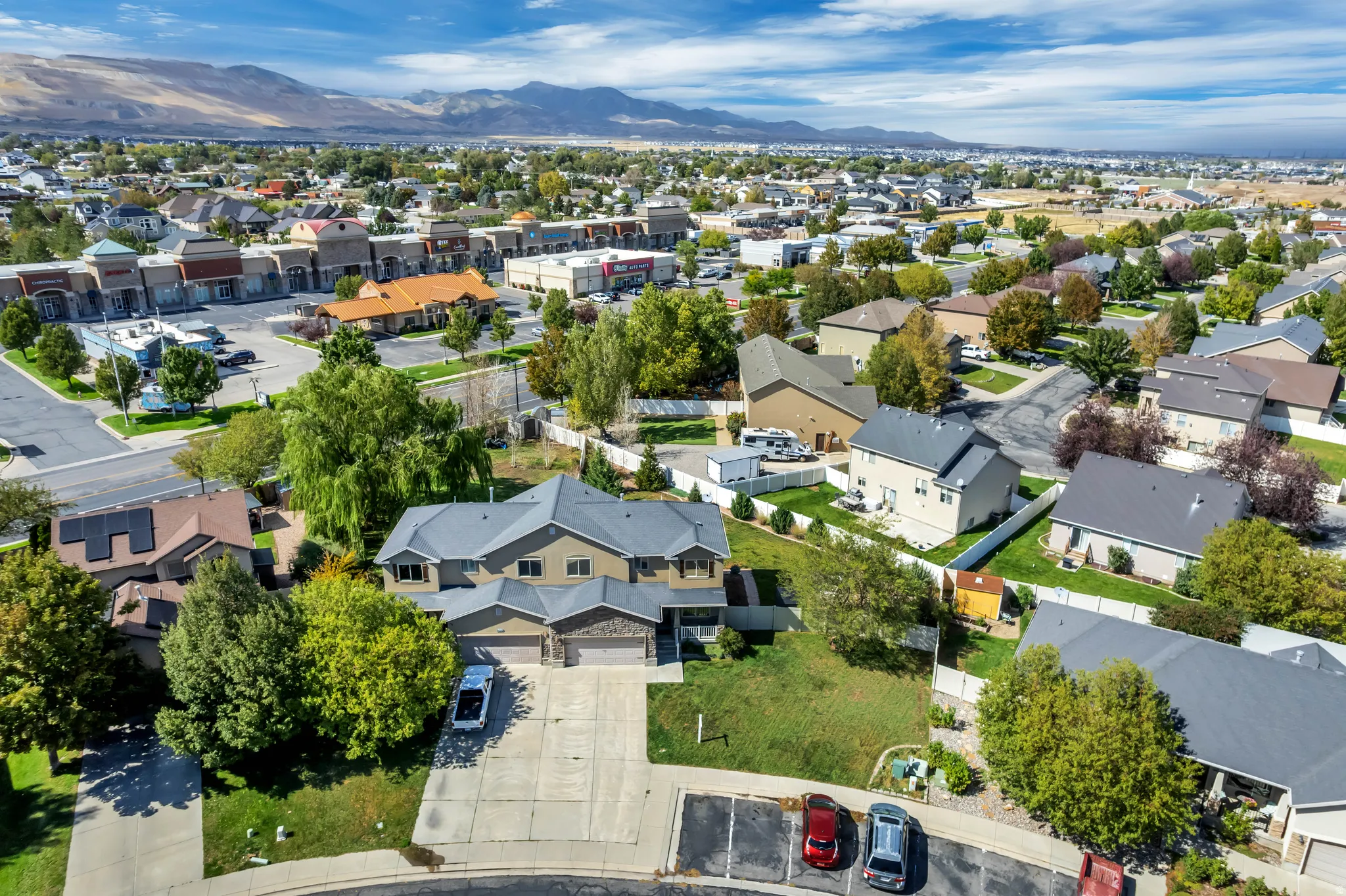 Residential street with houses featuring shingle roofs, mature trees, and paved driveways