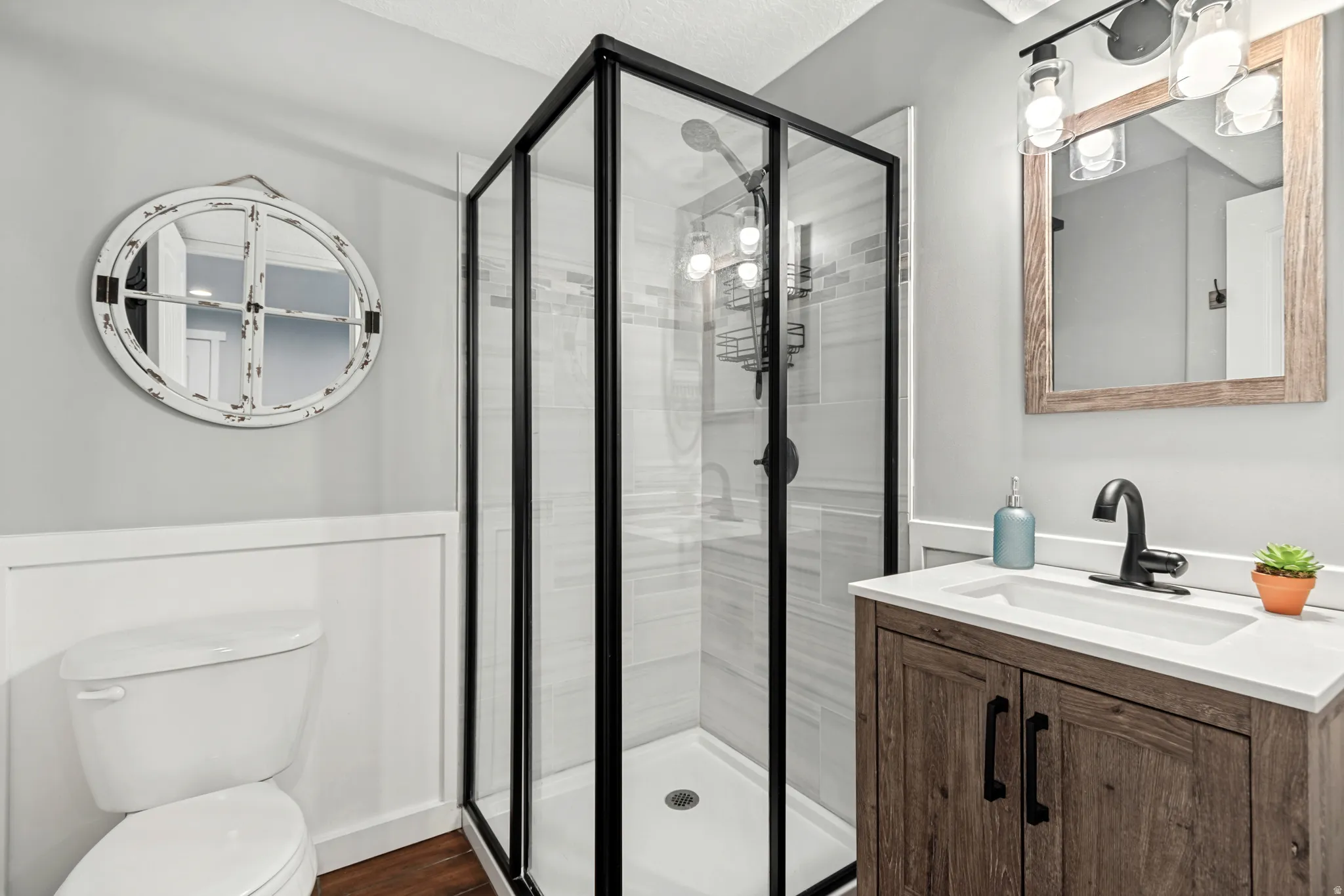 Glass-enclosed shower with black trim, wood-finish vanity with integrated sink, matte black faucet, and vertical wall paneling