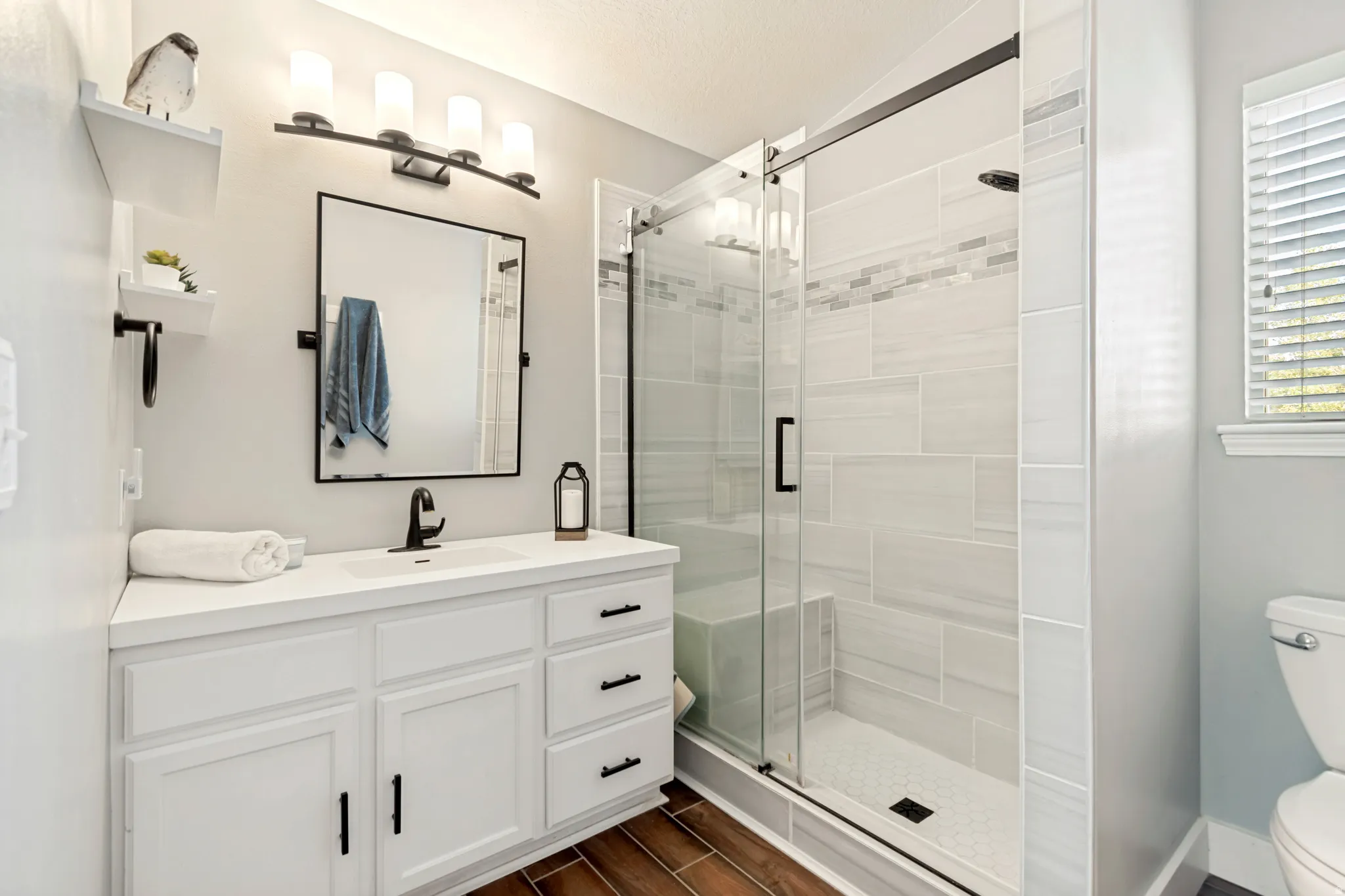 White vanity with a built-in sink and matte black hardware, framed mirror, and a walk-in shower featuring a glass enclosure and tiled walls