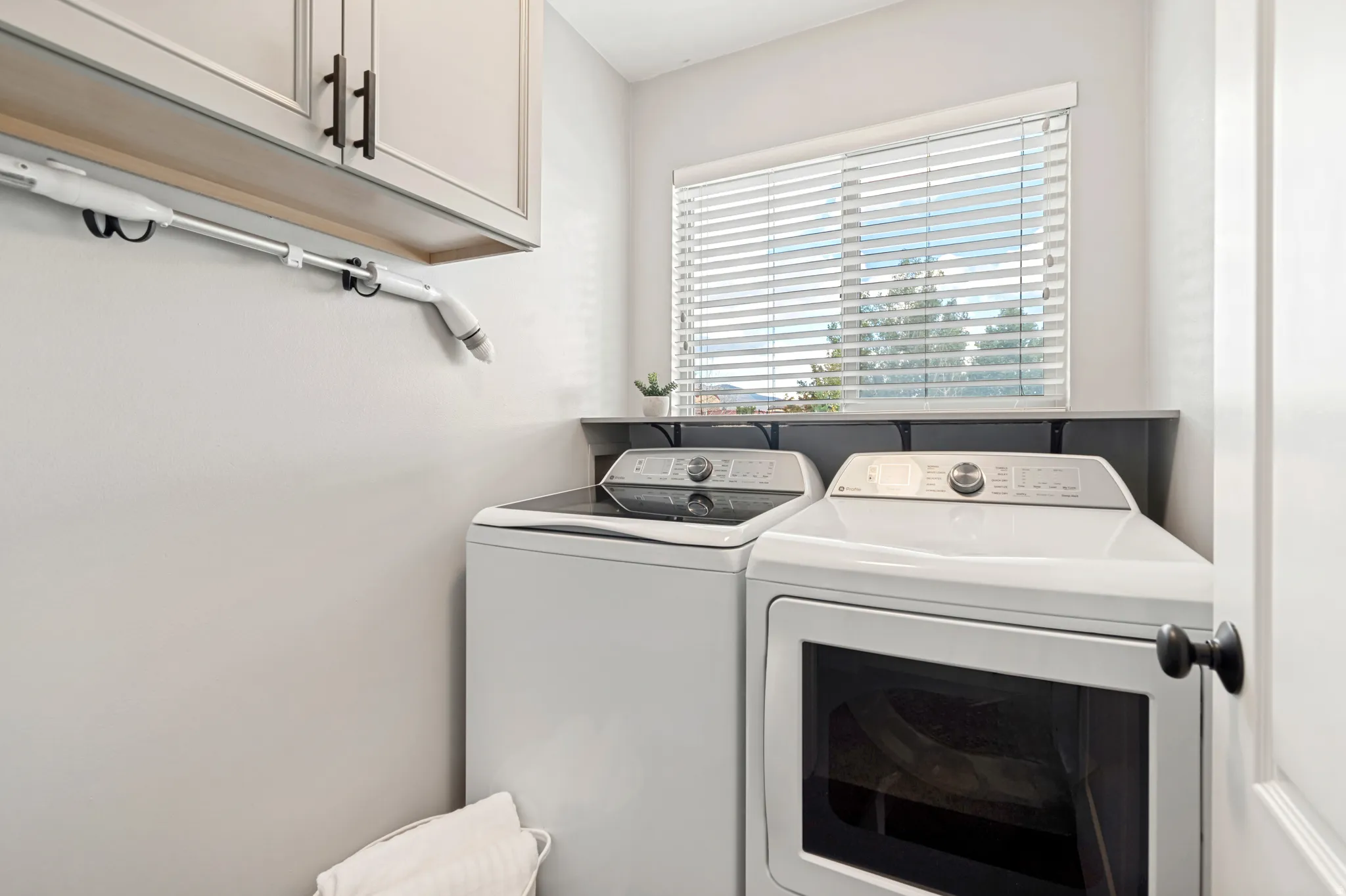 Window with horizontal blinds, built-in shelf, and upper cabinetry with black hardware