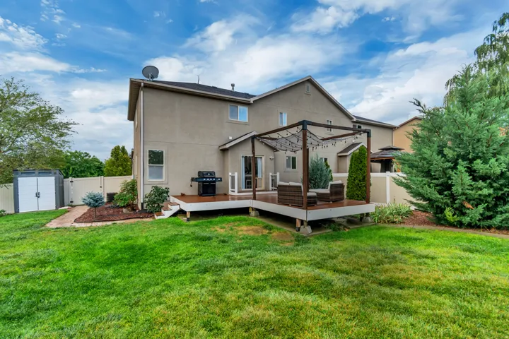 Expansive backyard featuring a manicured lawn, a raised wood deck with a pergola, and a detached storage shed