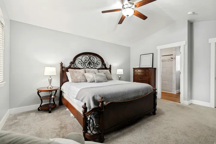 Vaulted ceiling with a ceiling fan, carpeted flooring, and an en-suite bathroom with tiled shower