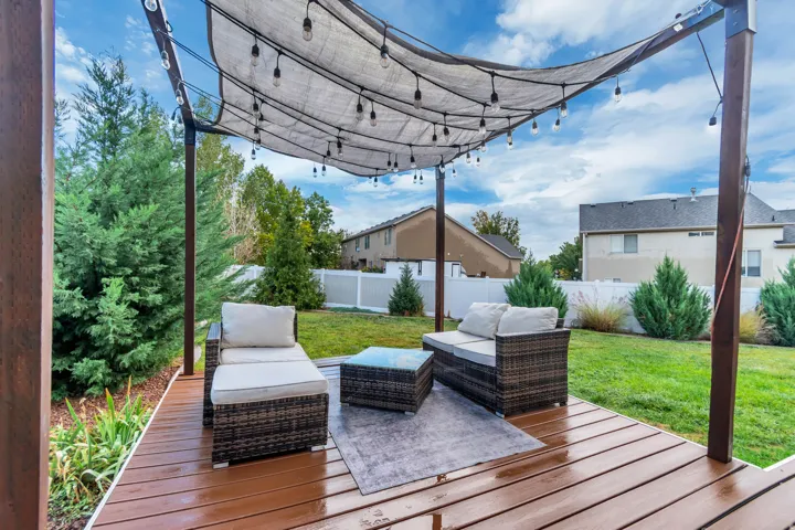 Expansive backyard featuring a wood-finish deck, shade structure with string lighting, manicured lawn, and privacy fencing