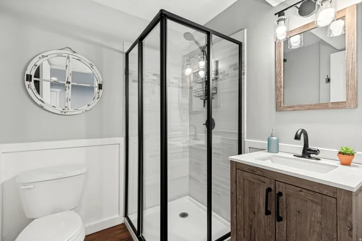 Glass-enclosed shower with black trim, wood-finish vanity with integrated sink, matte black faucet, and vertical wall paneling