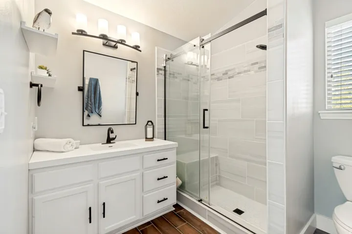 White vanity with a built-in sink and matte black hardware, framed mirror, and a walk-in shower featuring a glass enclosure and tiled walls