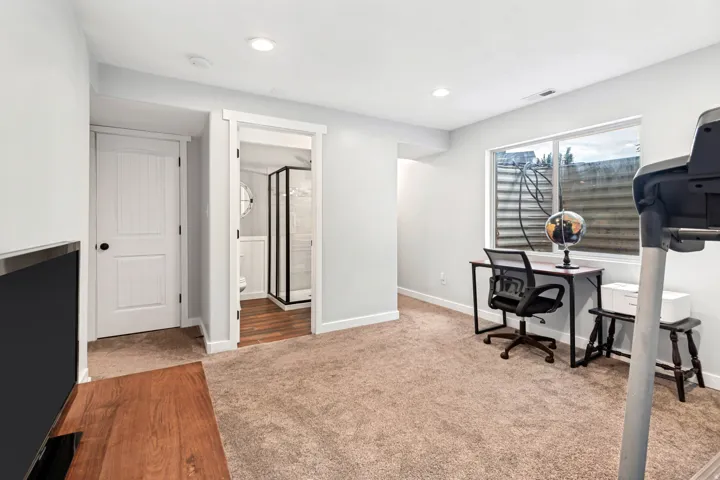 Recessed lighting, light-toned carpeting, wood-finish flooring, white paneled doors, and a transparent shower enclosure with a dark frame