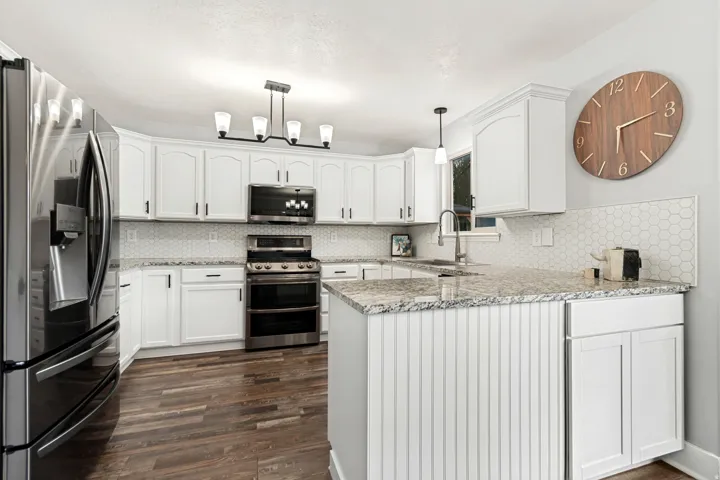 White cabinetry, stainless steel appliances, granite countertops, hexagon tile backsplash, and wood-finish flooring