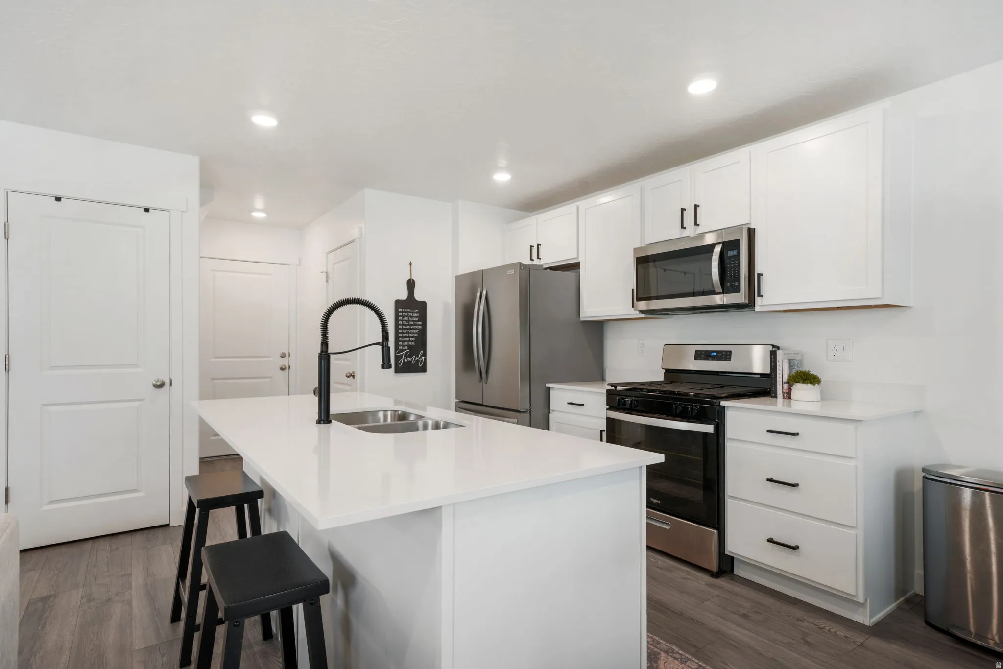 White cabinetry, stainless steel appliances, white countertops, wood-finish flooring, and a kitchen island with an integrated sink