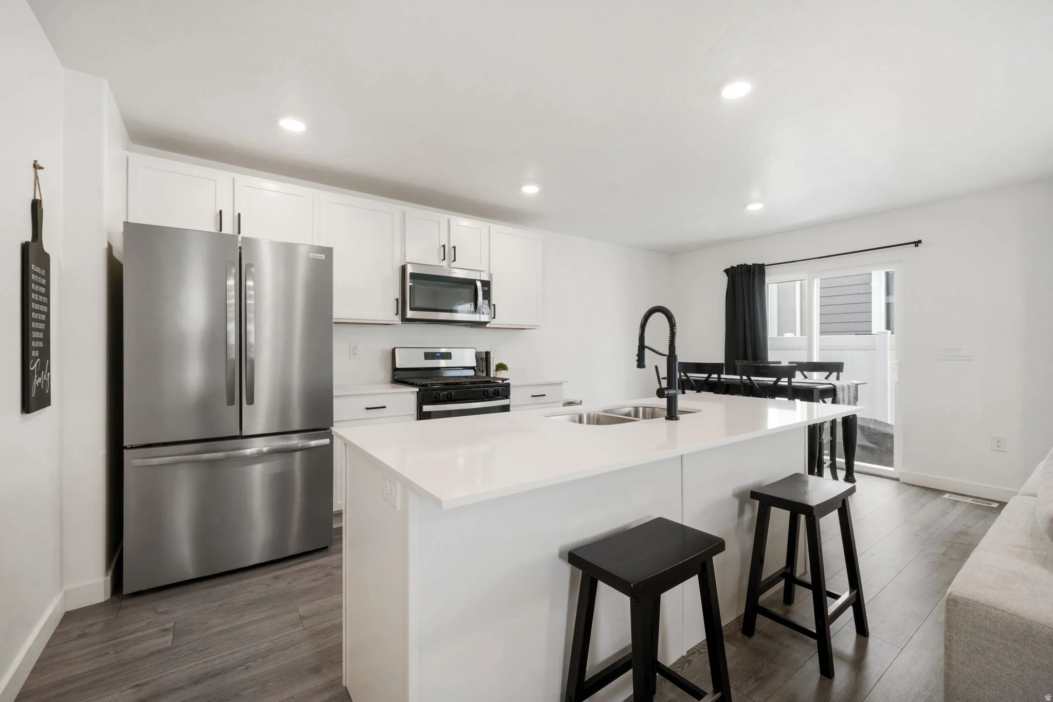 Modern kitchen featuring stainless steel French-door refrigerator, gas cooktop, and microwave with white cabinetry and quartz countertops