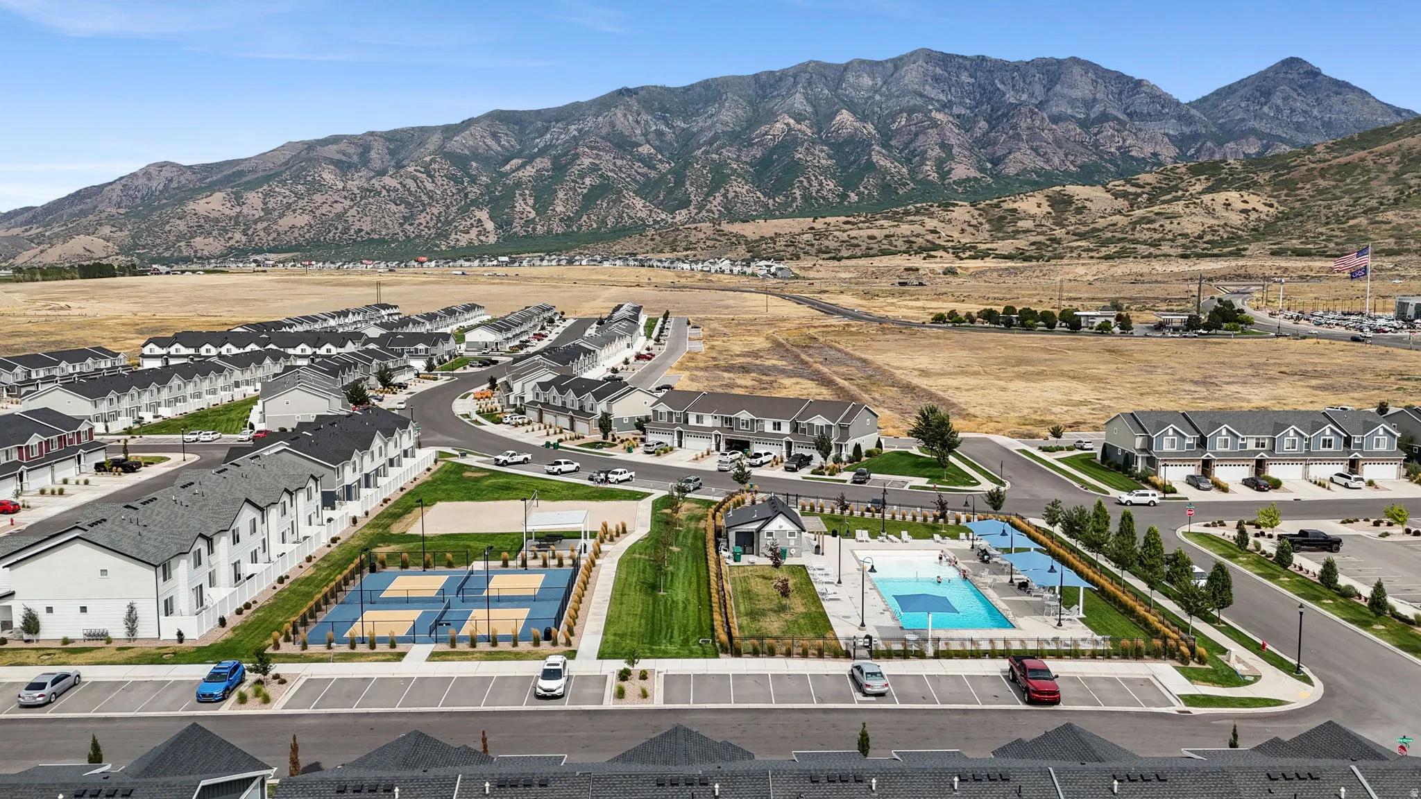 Aerial view of a master-planned residential community featuring multiple residential buildings with modern architecture, resort-style amenities including two sparkling pools and spa facilities, manicured landscaping with tree-lined pathways, and expansive