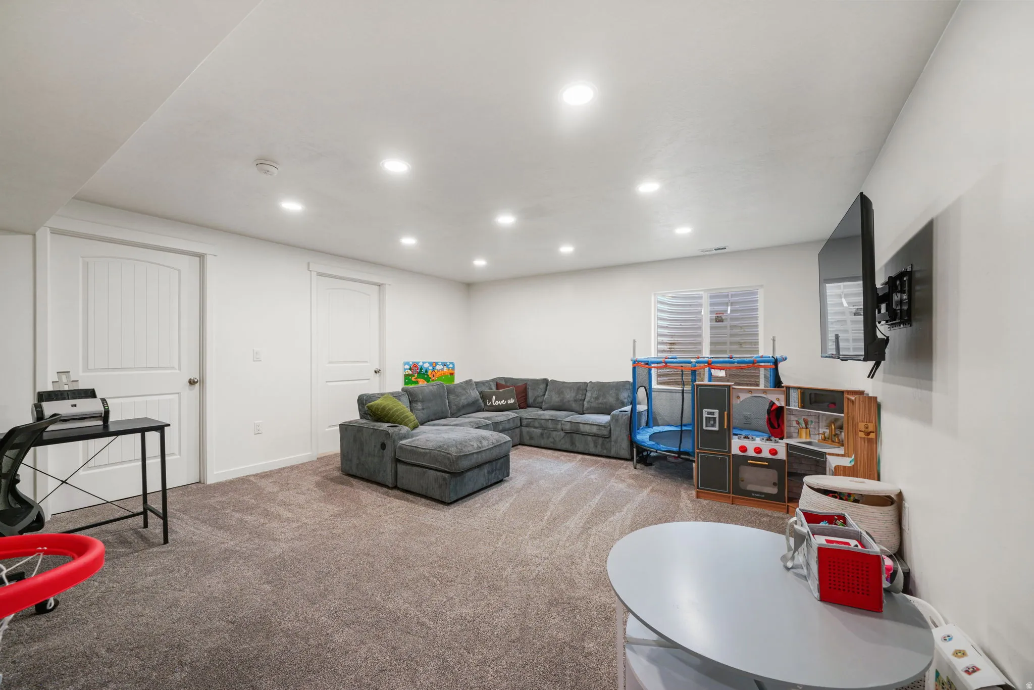 Recessed lighting, wall-mounted television, and neutral-toned carpeting enhance this versatile space
