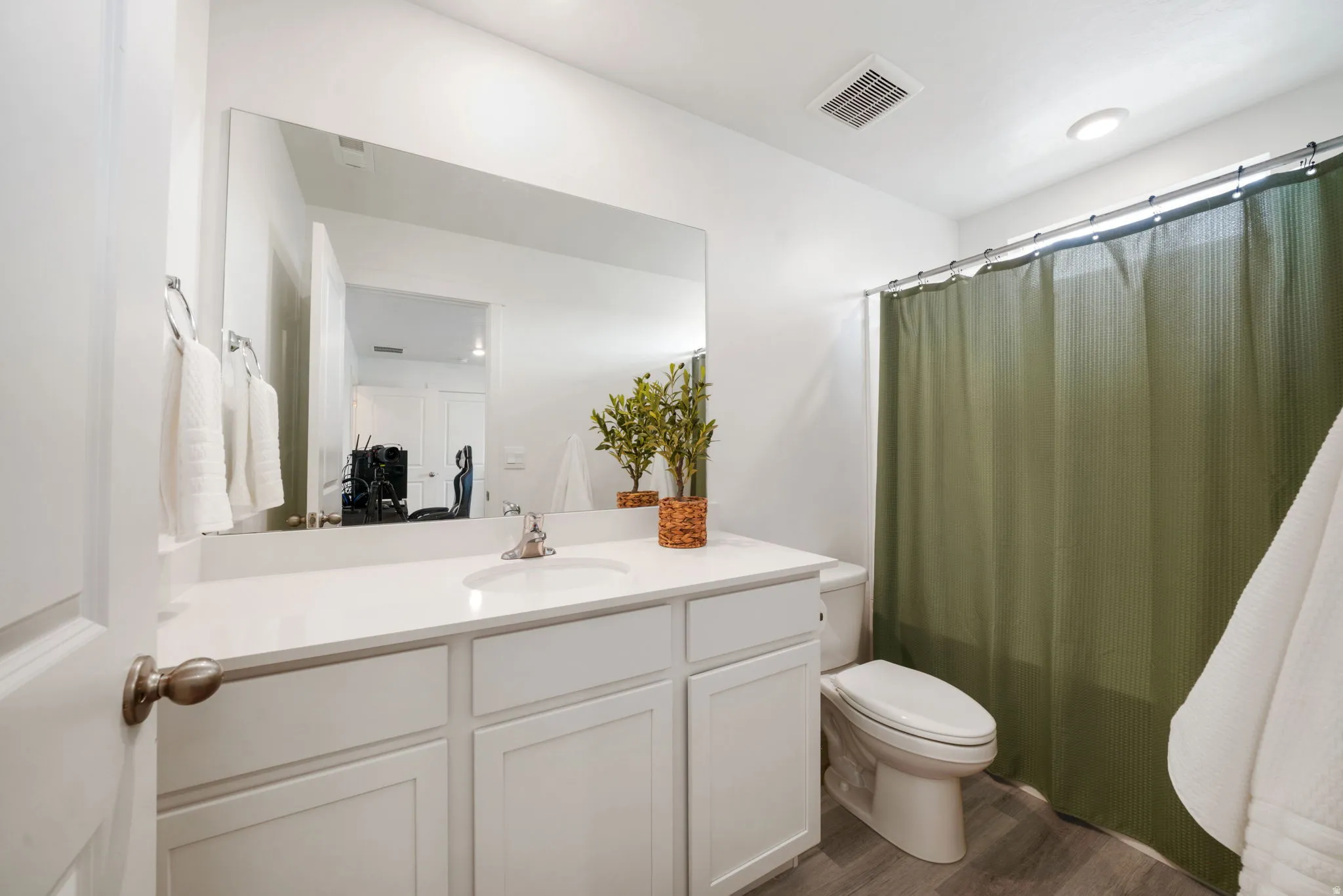 White vanity with panel cabinetry and integrated sink, expansive wall mirror, contemporary toilet, and wood-finish flooring