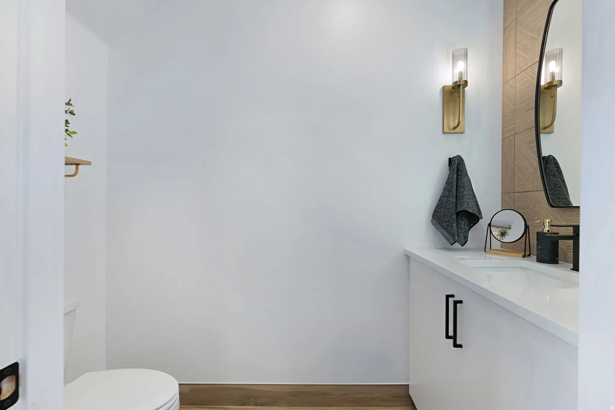 White vanity with integrated sink, black hardware, wall-mounted sconces, and wood-finish flooring