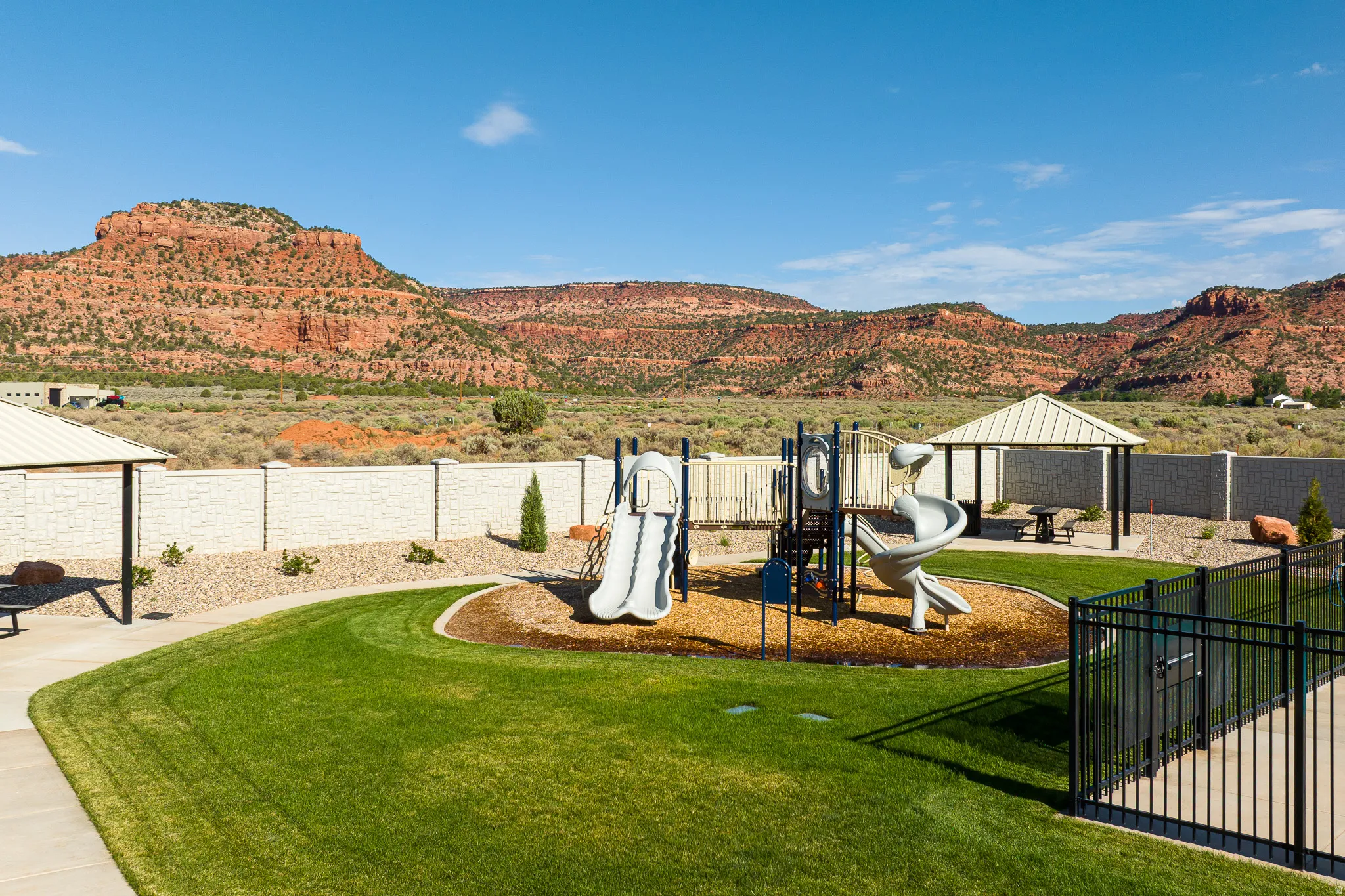 Landscaped common area with a playground structure, two covered gazebos, and a decorative stone wall