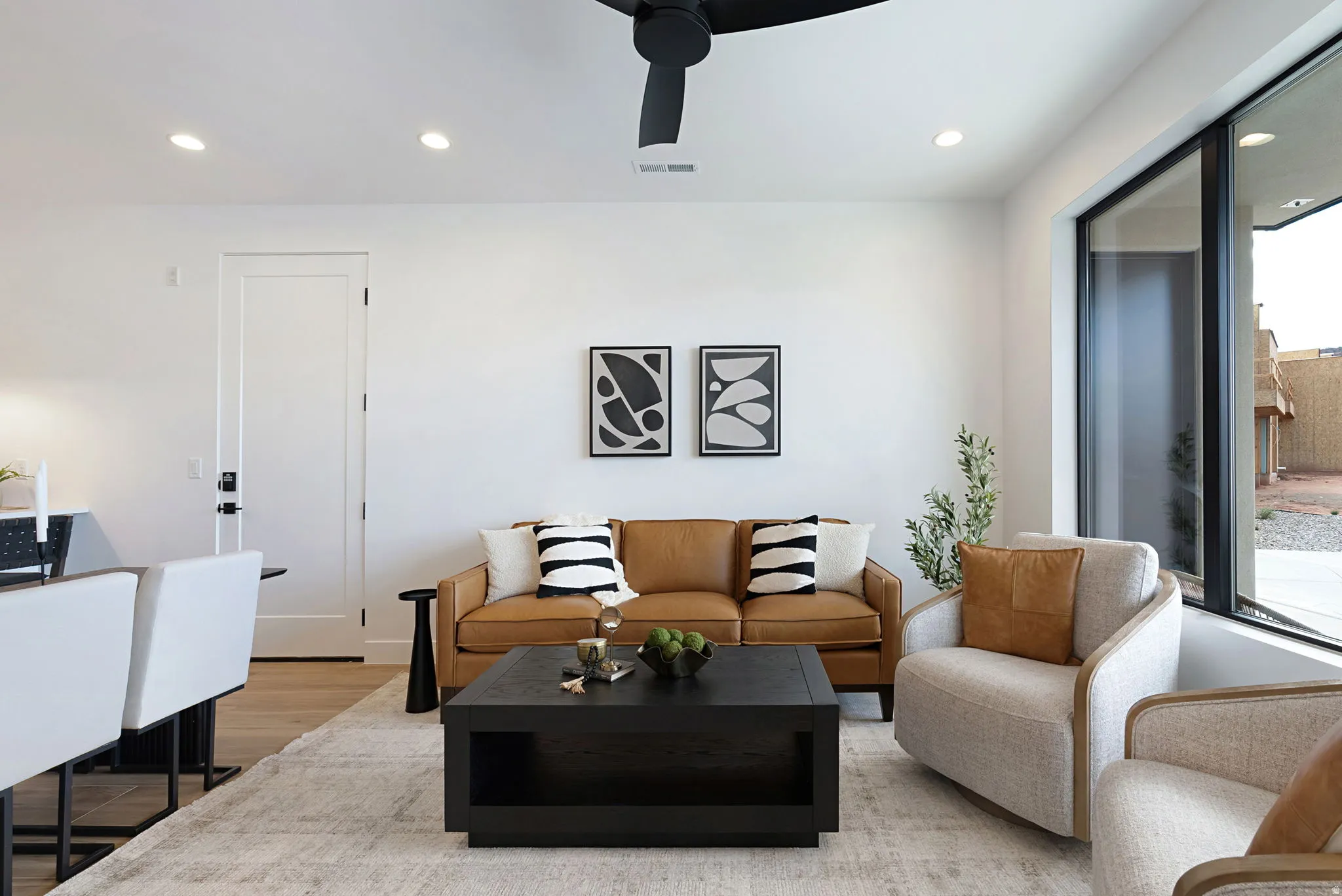 Recessed ceiling lighting, a modern ceiling fan, large windows, wood-finish flooring, and a white interior door with black hardware