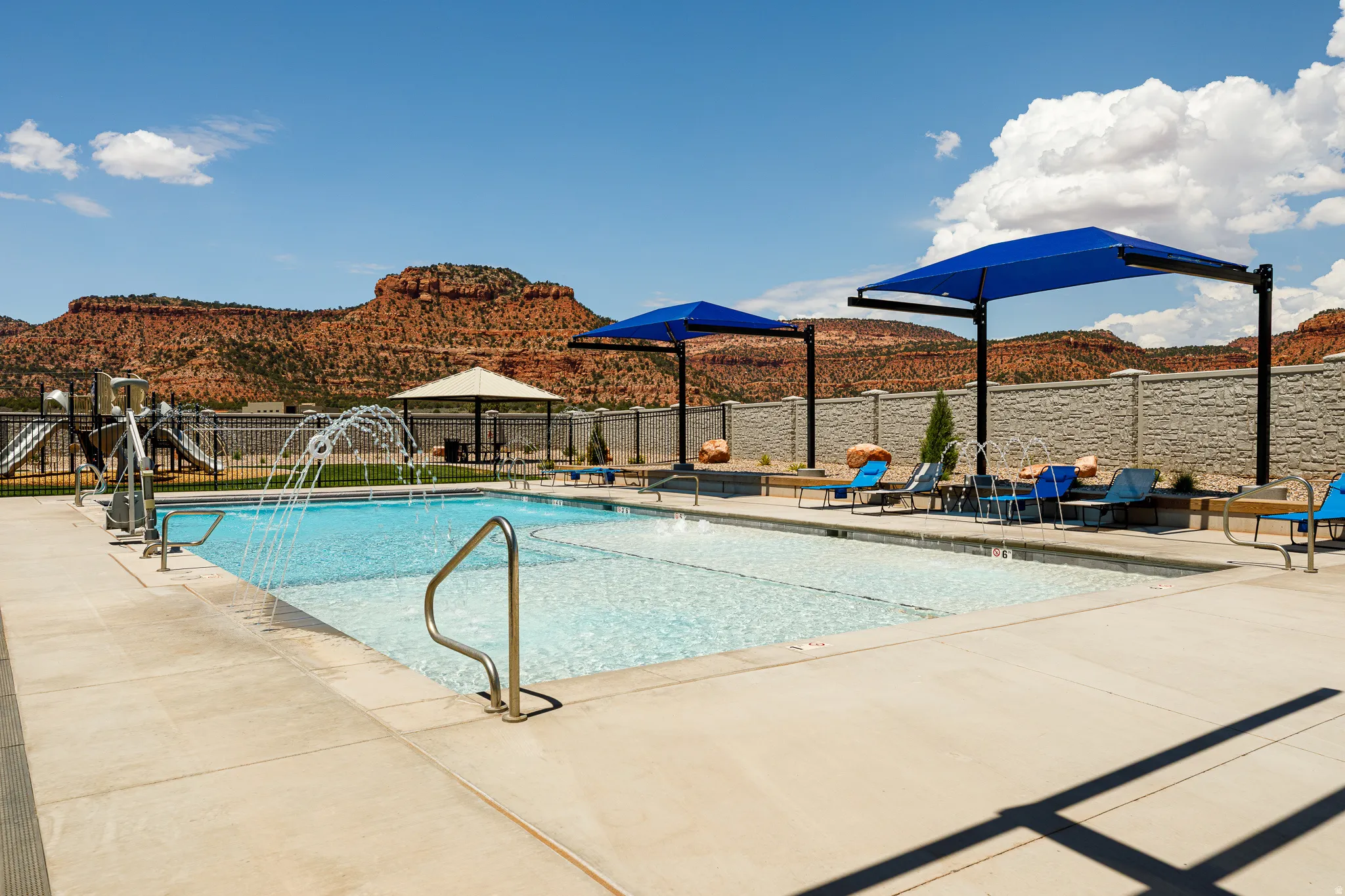 Expansive swimming pool with integrated water feature, perimeter concrete decking, two large shade structures, and a dedicated wading area