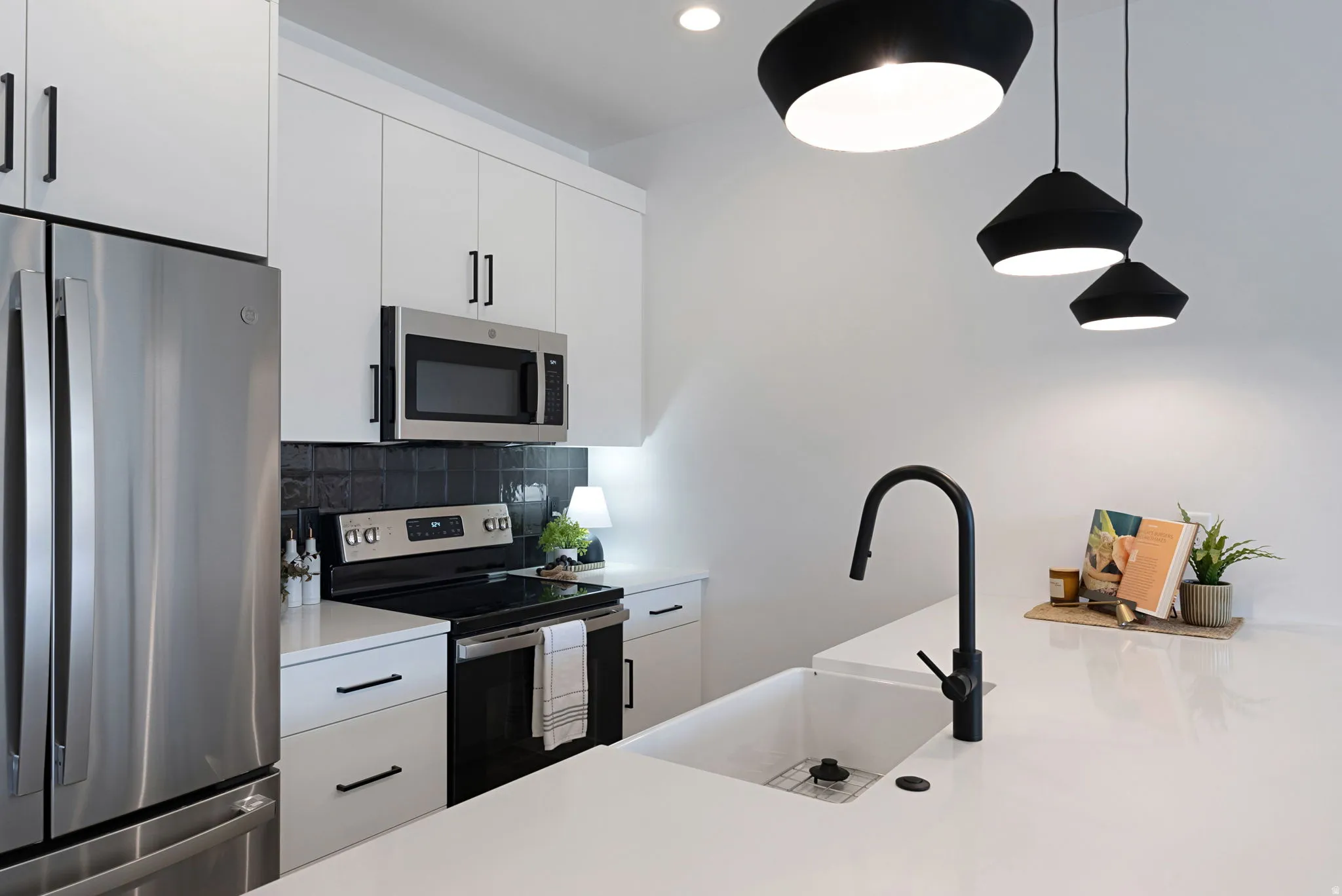 Stainless steel refrigerator, built-in microwave, black flat-top range, white cabinetry with black hardware, and an undermount sink with a matte black faucet