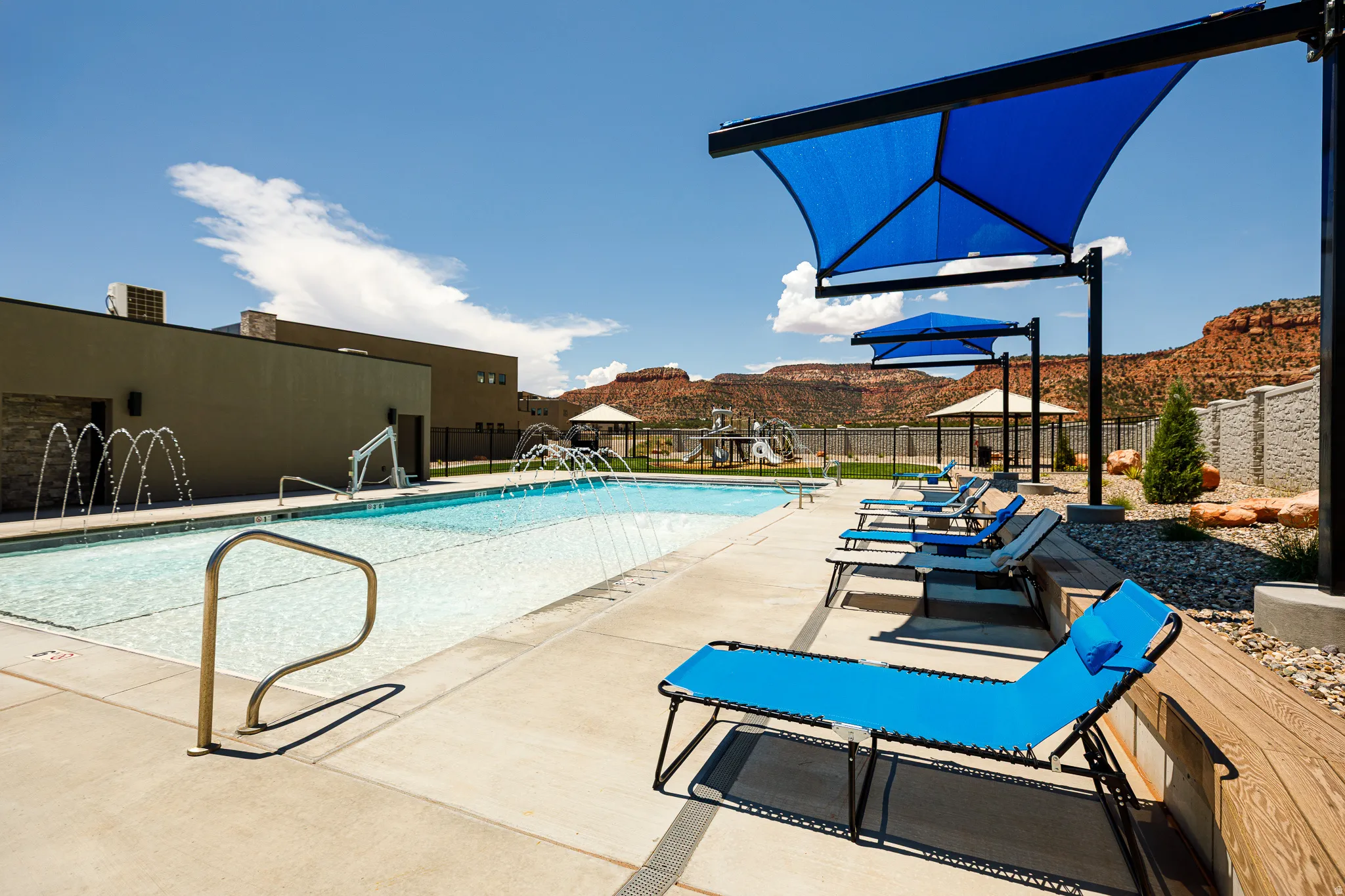 Community swimming pool with water features, concrete decking, and multiple shade structures
