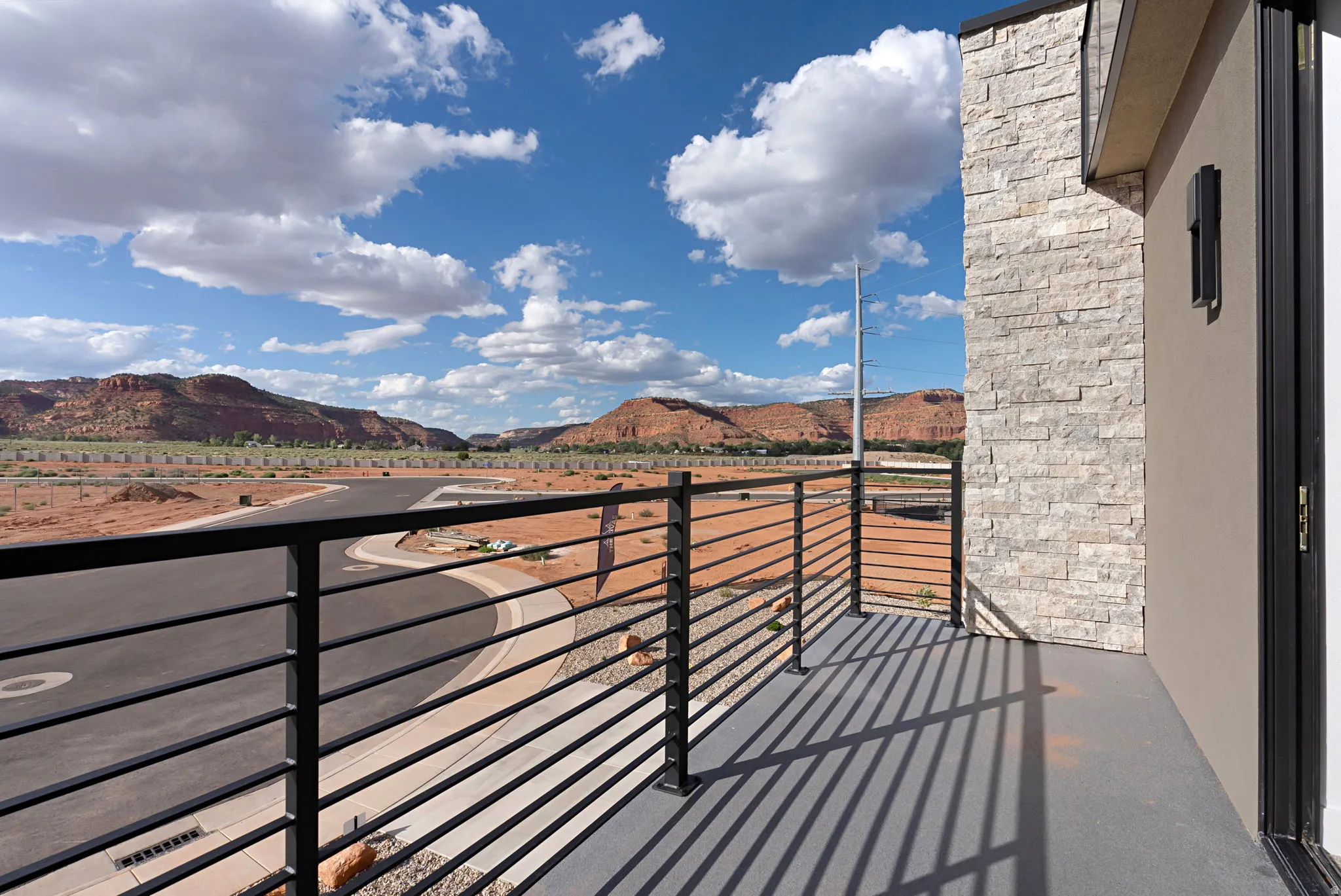 Balcony featuring a black metal horizontal railing, light stacked stone facade, and exterior lighting fixture