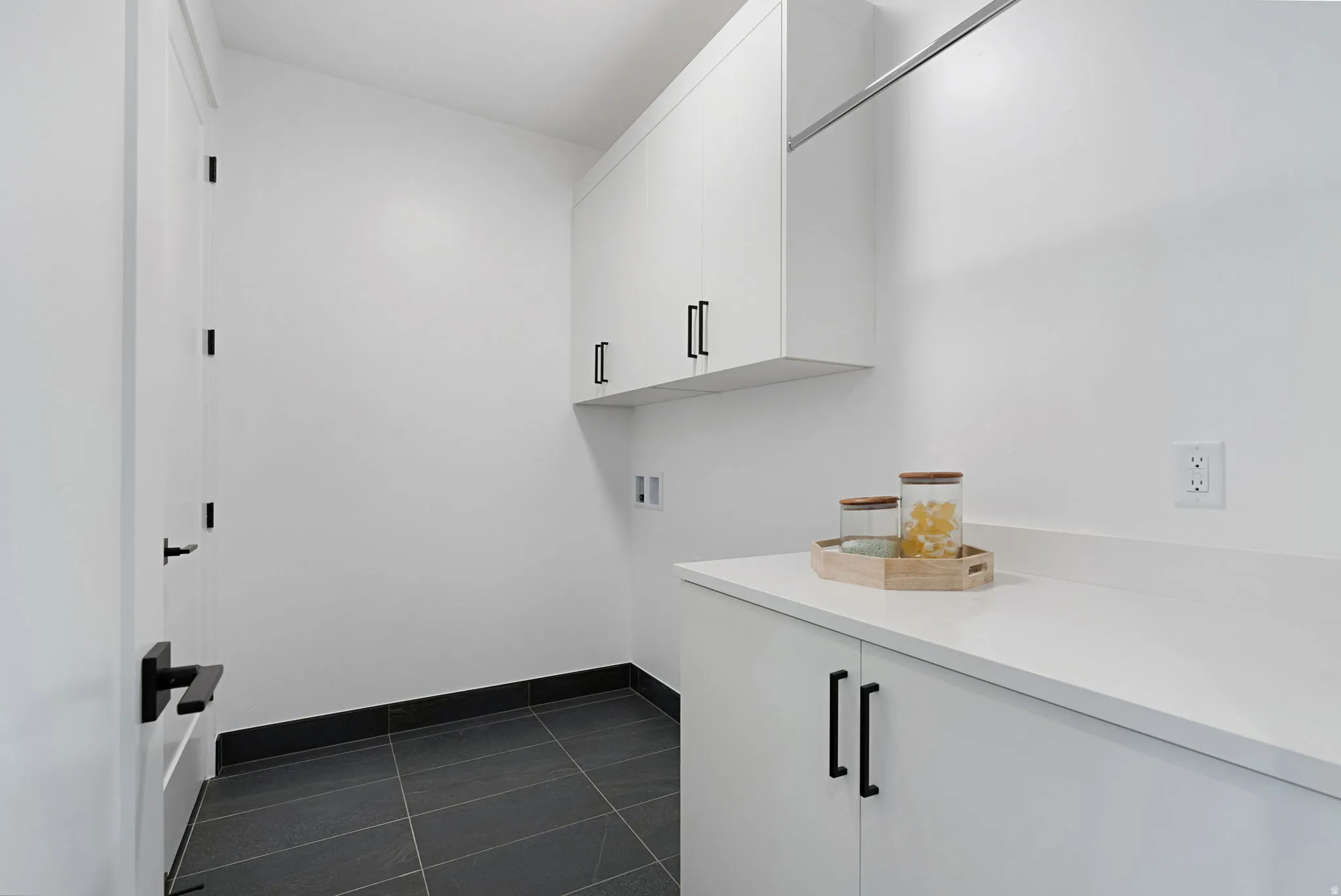 White cabinetry with matte black hardware, white countertop, dark tile flooring, and a built-in hanging rod