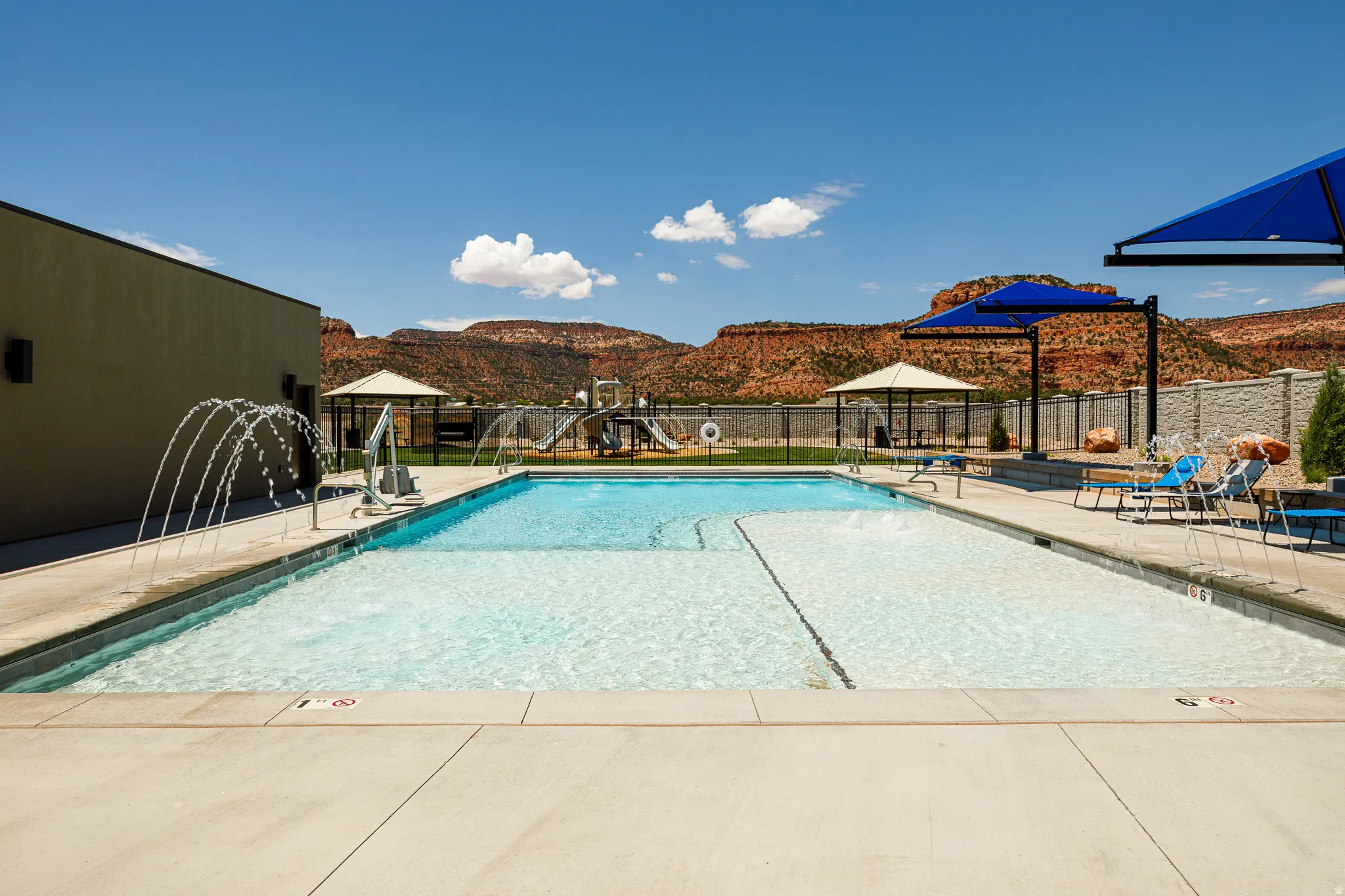 Expansive swimming pool with water features, sun shelf, and surrounding concrete decking
