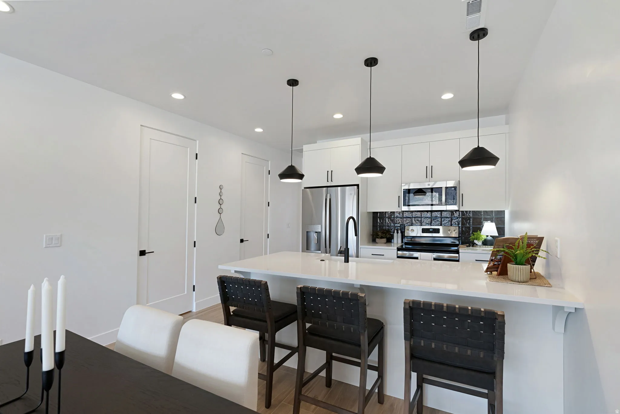 White cabinetry and integrated stainless steel appliances, a kitchen island with a white countertop, and pendant lighting fixtures
