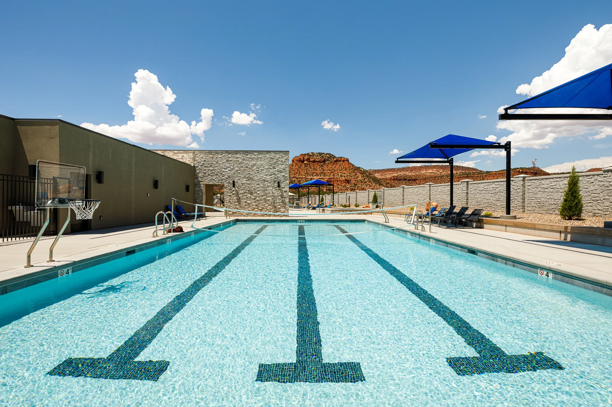 Lap pool featuring lane markers, poolside basketball hoop, and shaded lounge areas