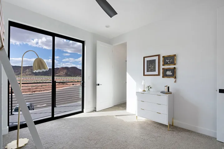 Sliding glass door with black trim, direct access to an outdoor balcony, light-colored carpeting, white walls, and a ceiling fan