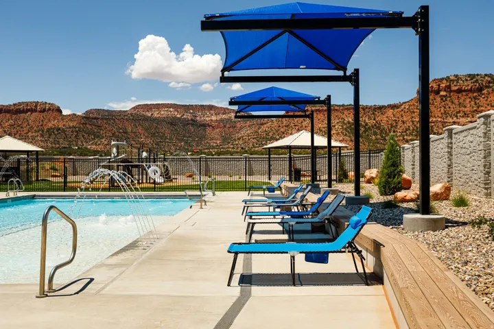 Resort-style pool with water features, shaded lounge areas, wood-finish bench seating, and a structured privacy wall