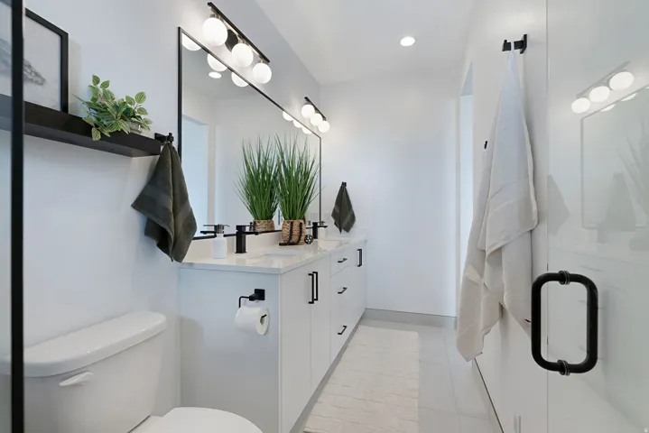 Dual vanity with matte black fixtures, white cabinetry, long mirror, and recessed lighting