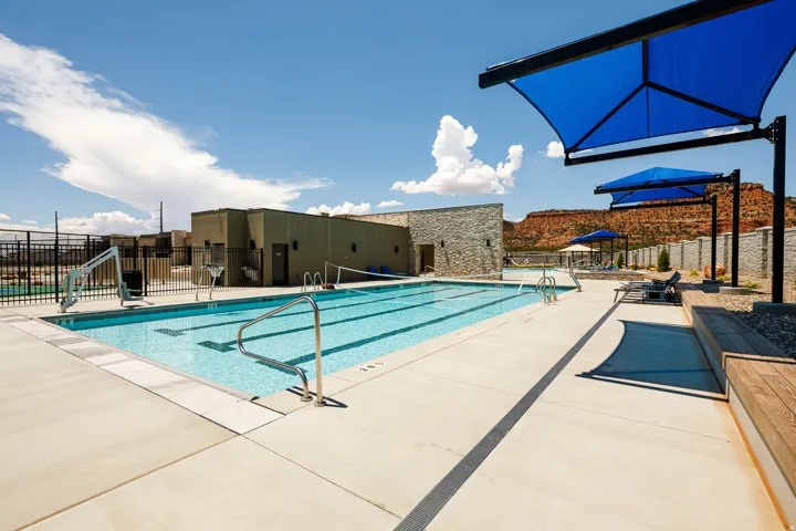 Outdoor swimming pool with concrete decking, blue shade structures, and built-in wood bench seating