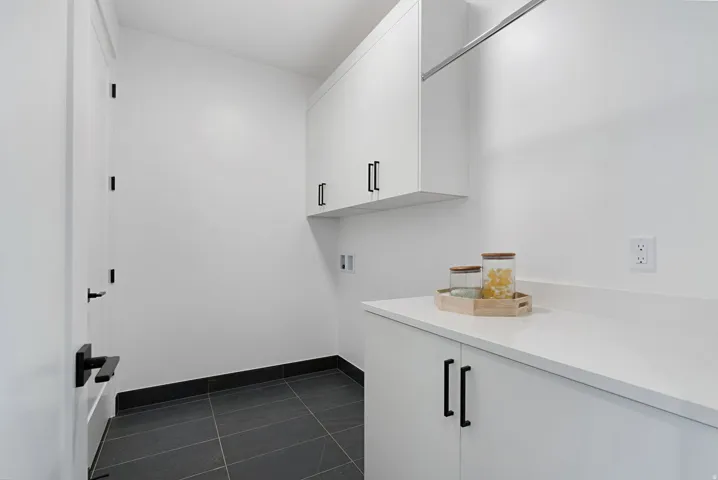 White cabinetry with matte black hardware, white countertop, dark tile flooring, and a built-in hanging rod