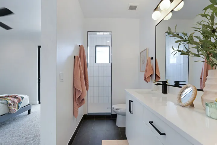 Modern bathroom featuring a white vanity with integrated sink, black hardware, a rectangular mirror with black trim, and a shower with white vertical subway tile