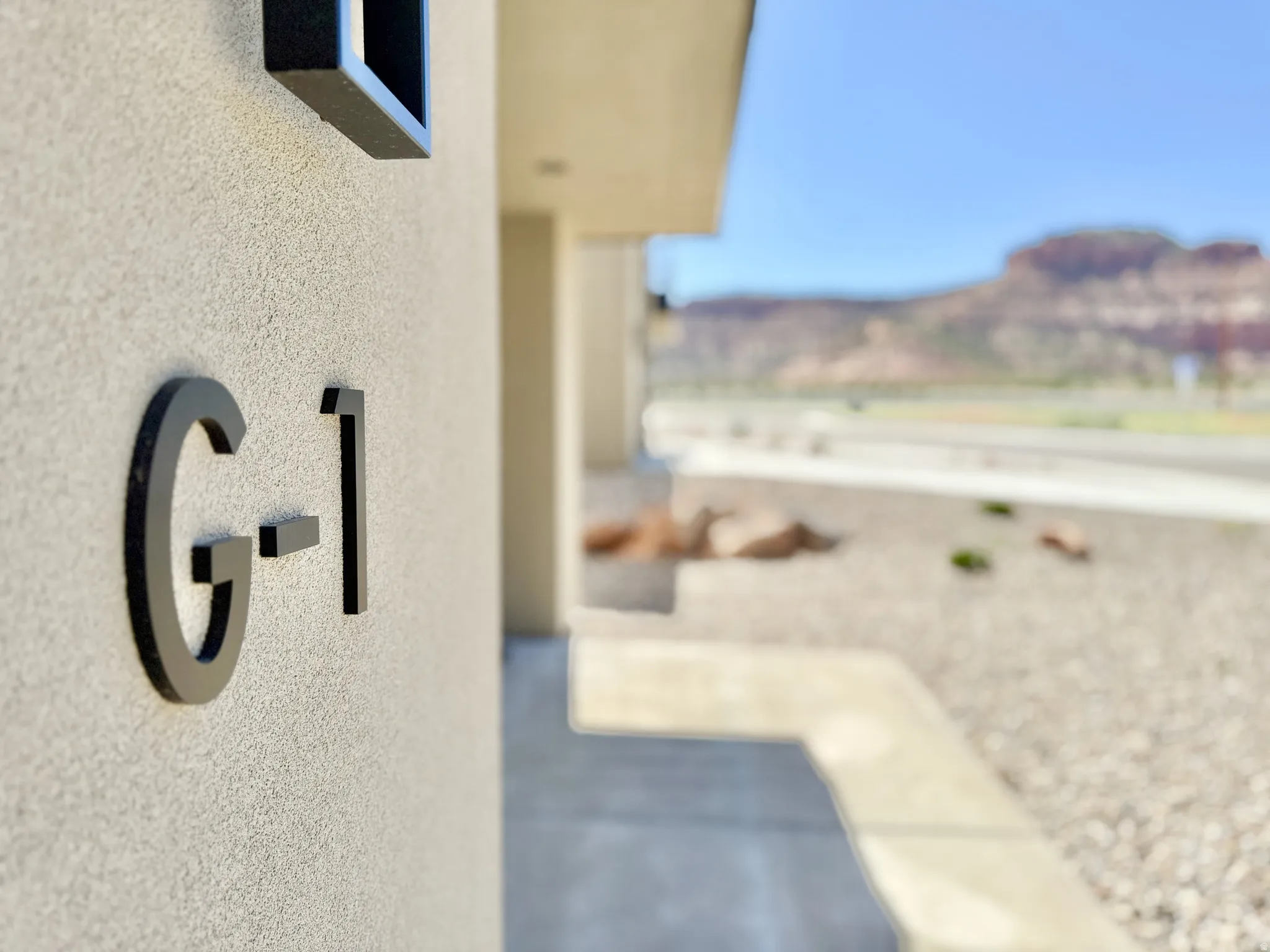 Exterior wall with textured finish, modern address numbers, concrete pathway, and arid landscaping