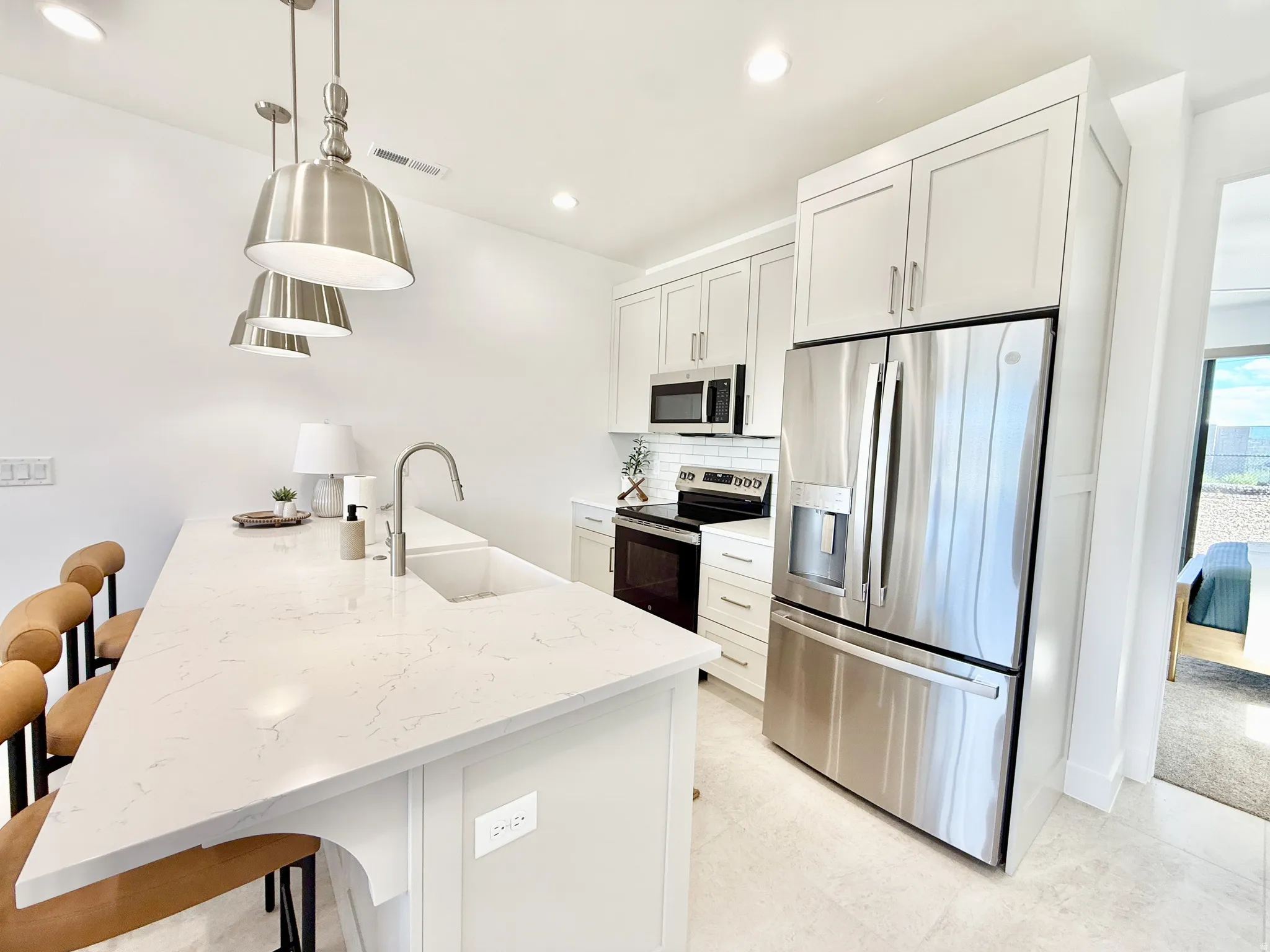 Kitchen featuring a substantial island with a composite countertop and integrated sink, stainless steel appliances, light cabinetry, and recessed lighting