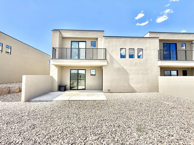 Modern stucco exterior featuring a second-story balcony with metal railing, ground-level patio, and sliding glass doors