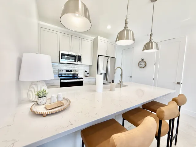 Kitchen featuring light-toned cabinetry, stainless steel appliances, a subway tile backsplash, a large island with a surface, and pendant lighting