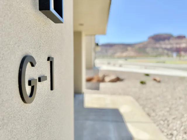 Exterior wall with textured finish, modern address numbers, concrete pathway, and arid landscaping