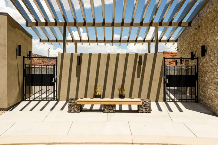 Pergola structure, stone veneer accent wall, stucco exterior finish, concrete patio, black metal gates