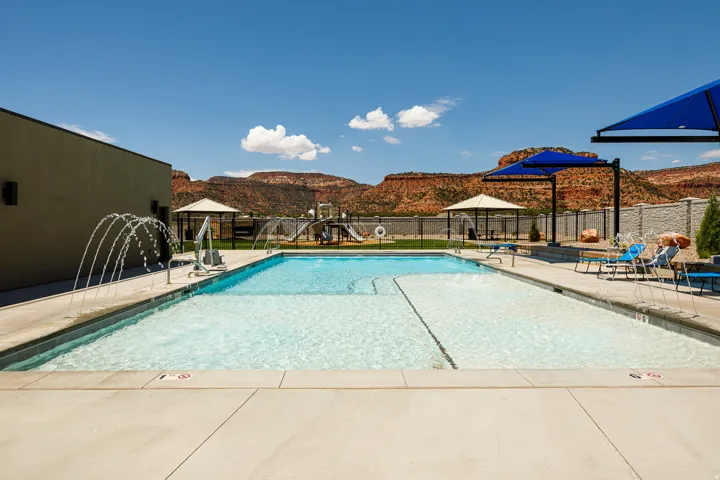 Expansive pool area featuring a large swimming pool with water features, a shaded seating area, and a playground