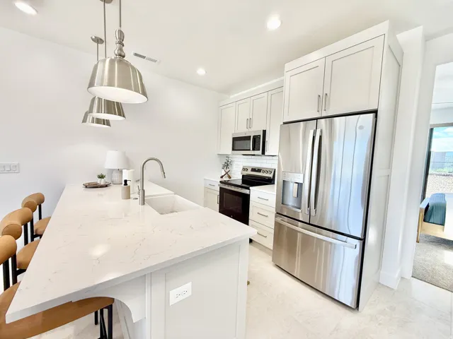 Kitchen featuring a substantial island with a composite countertop and integrated sink, stainless steel appliances, light cabinetry, and recessed lighting