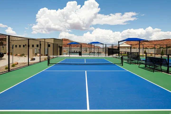 Blue and green sport court, chain link fencing, modern amenity building, shaded seating areas, and distant red rock landscape