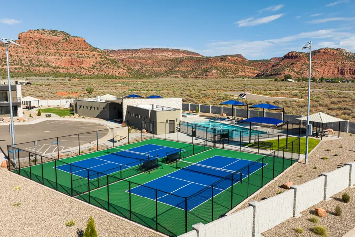 Community amenities featuring two pickleball courts, a fenced swimming pool area, a shaded gazebo, and a modern clubhouse building