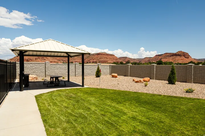 Lawn area with a paved walkway, a metal-roofed gazebo, a decorative stone wall, and a gravel landscape