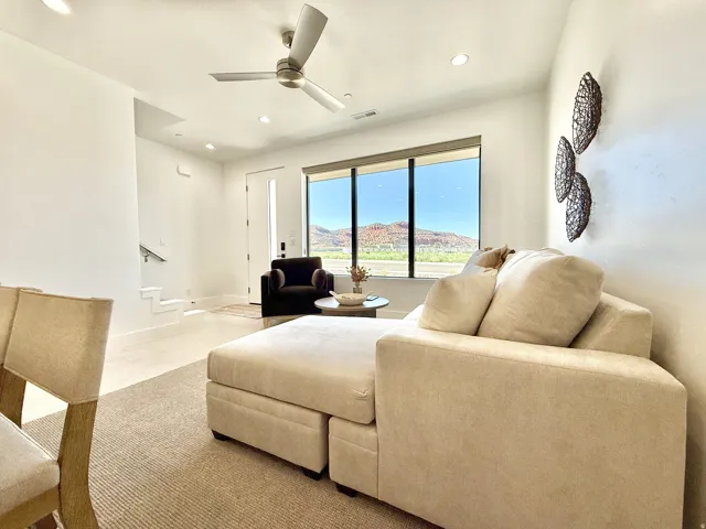 Open-concept living space featuring a ceiling fan with integrated lighting, large windows, recessed lighting, and a modern staircase with a metal handrail