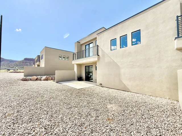 Contemporary stucco exterior with dark-framed windows, a private balcony with horizontal railings, and a ground-level patio
