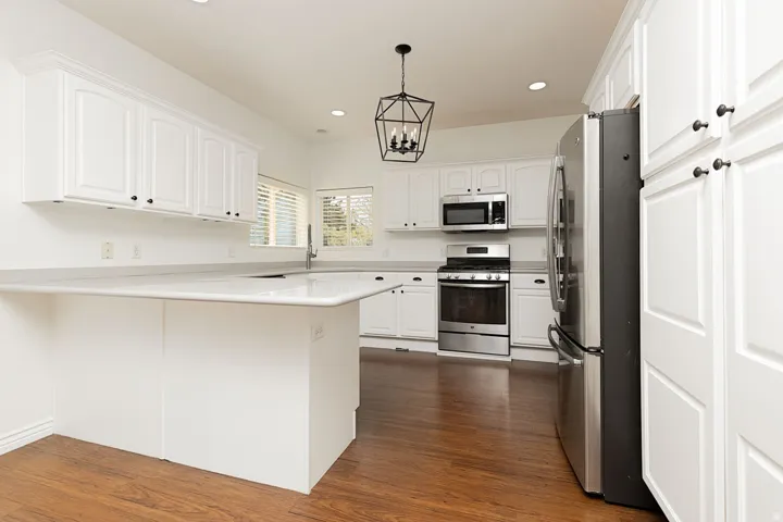 Expansive kitchen featuring white cabinetry, light-toned countertops, wood-finish flooring, a stainless steel range, and a geometric pendant light fixture