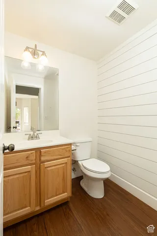 Wood-finish flooring with a white vanity featuring a ceramic sink, brushed nickel faucet, and a wall-mounted light fixture